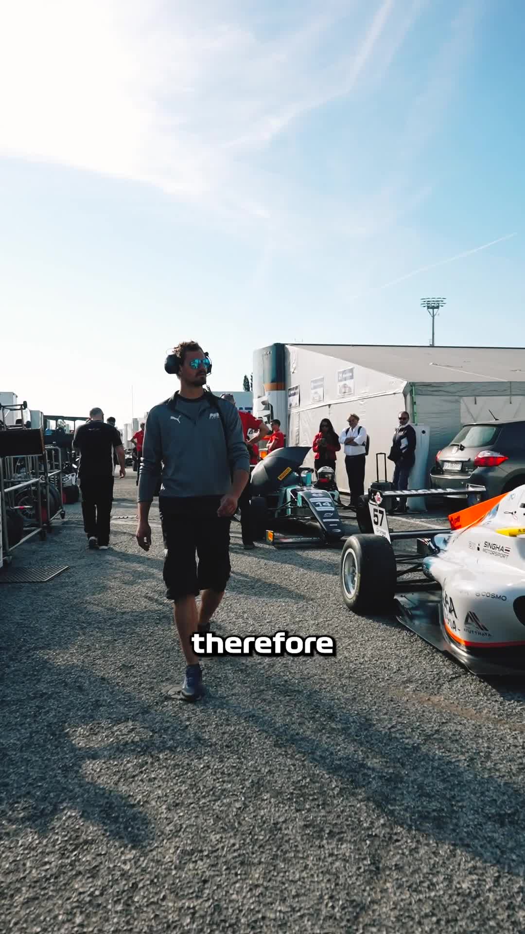 Team member walking through the race paddock past a Formula 4 car